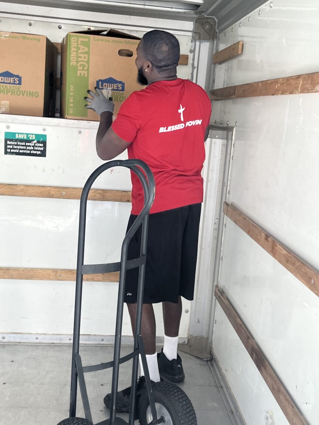 A person in a red shirt loads boxes labeled Lowe's into a moving truck, with a dolly nearby.