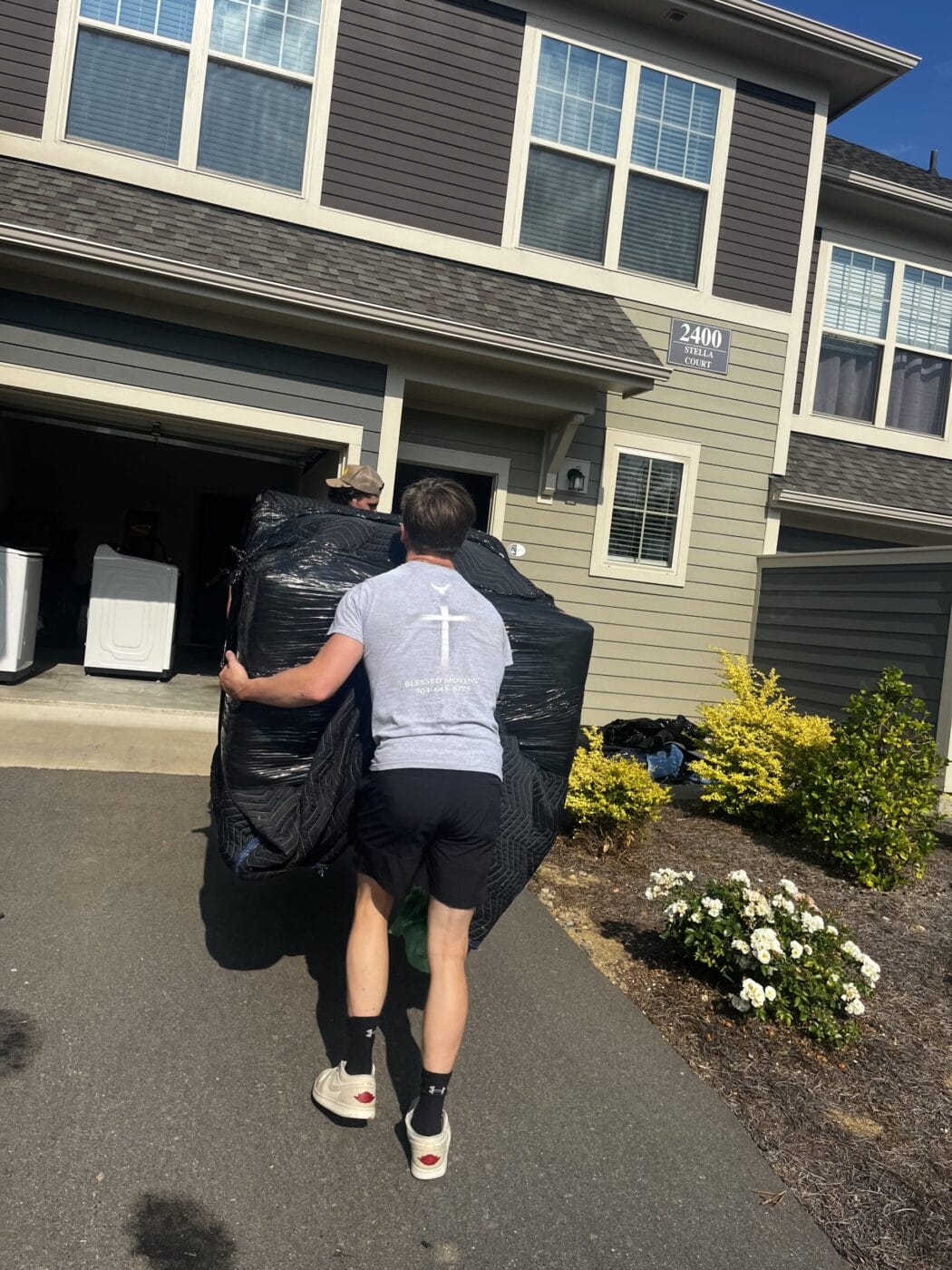 Person carrying a large, wrapped object towards a residential house on a sunny day.